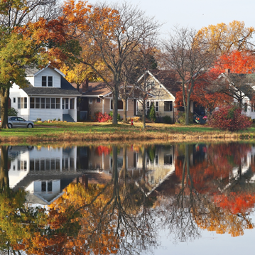 a lake surrounded by trees with houses in the background